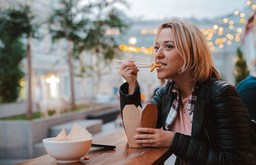 European blonde girl eating rice Pho Bo with wooden sticks table street Vietnamese cafe in Moscow.