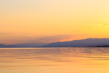 Beautiful sunset on a lake in the mountains. Kyrgyzstan, Issyk-Kul Lake. Bright sky, background in warm colors.