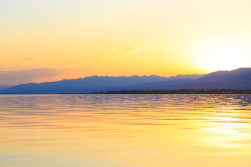 Fototapeta premium Beautiful sunset on a lake in the mountains. Kyrgyzstan, Issyk-Kul Lake. Bright sky, background in warm colors.