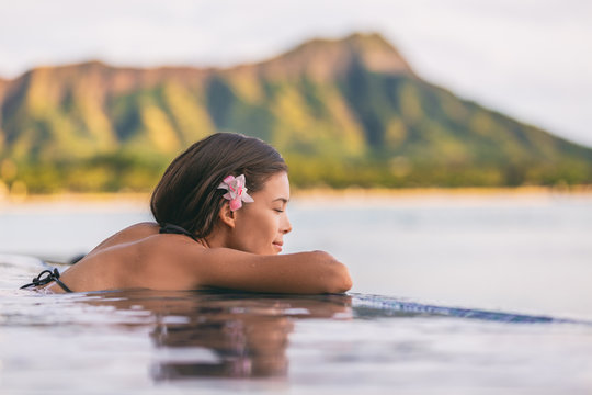 Luxury resort wellness pampering spa lifestyle Asian woman relaxing in infinity swimming pool of outdoor hotel on Waikiki beach, Honolulu, Hawaii travel.