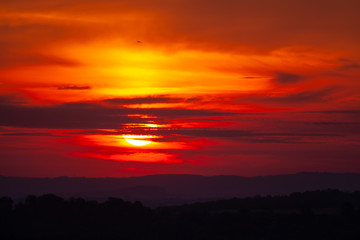 Fototapeta na wymiar Red sunrise over hills with small wind power plants on horizon
