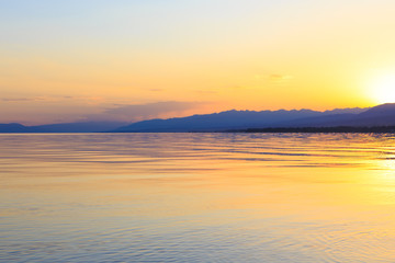 Beautiful sunset on a lake in the mountains. Kyrgyzstan, Issyk-Kul Lake. Bright sky, background in warm colors.
