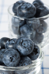 Blueberries are in a small glass cup placed on a white tablecloth with blue lines.