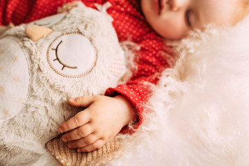 Cute little baby girl sleeping on light blanket with plush owl, little hand on fron view