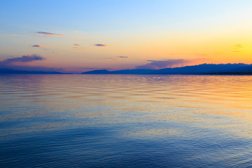 Beautiful sunset on a lake in the mountains. Kyrgyzstan, Issyk-Kul Lake. Bright sky, background in warm colors.