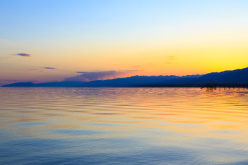 Beautiful sunset on a lake in the mountains. Kyrgyzstan, Issyk-Kul Lake. Bright sky, background in warm colors.