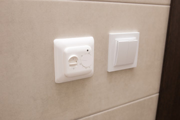 White temperature controller of a warm floor on a gray wall.