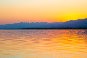 Obraz premium Beautiful sunset on a lake in the mountains. Kyrgyzstan, Issyk-Kul Lake. Bright sky, background in warm colors.