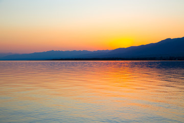 Obraz premium Beautiful sunset on a lake in the mountains. Kyrgyzstan, Issyk-Kul Lake. Bright sky, background in warm colors.