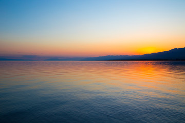 Beautiful sunset on a lake in the mountains. Kyrgyzstan, Issyk-Kul Lake. Bright sky, background in warm colors.