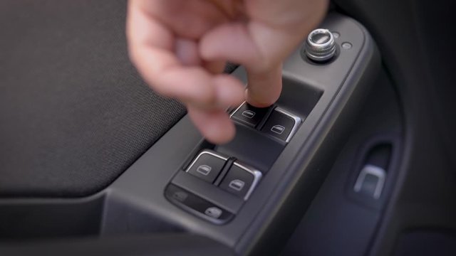 driver is pressing buttons of window switches with remote control inside modern car, closeup view of hand