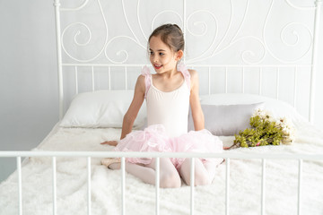 Selective focus happy little young girl ballet dancer in pink ballet dress sitting on white bed at bedroom and thinking a fun idea. Pretty ballerina child girl have a dreaming good idea inspiration. © CandyRetriever 