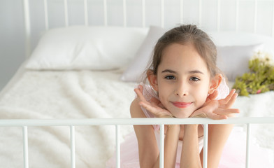 Obraz na płótnie Canvas Selective focus happy young little girl face in pink ballet dress lying down on white bed in bedroom and smile. Smiling cheerful pretty ballerina child girl with a dreaming inspiration in her eyes