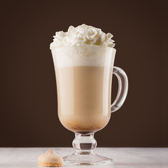 Morning cappuccino coffee in exquisite transparent glass with whipped cream, cookies in dark brown interior, square.