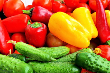 Heap of green cucumbers, large red and yellow sweet peppers and red ripe tomatoes. Close up. Vegetable background