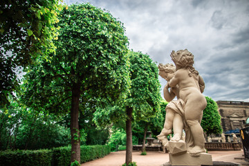 Fototapeta na wymiar Dresden, Germany - may 27, 2019. Sculpture of small cupids near alley of green trees, Zwinger palace