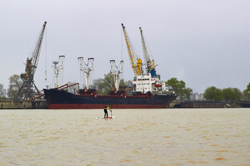 Man on stand up paddle boards (SUP) paddling along the loading area of the port on the Danube river