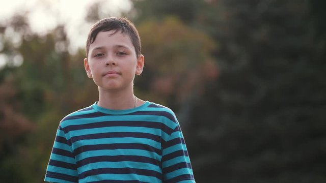Nice brunet boy standing and smiling in a green park in summer in slow motion