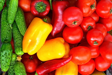 Heap of green cucumbers, large red and yellow sweet peppers and red ripe tomatoes. Vegetable background. Top view