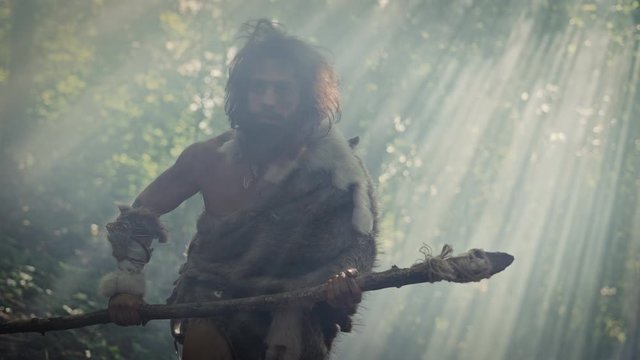 Portrait of Primeval Caveman Wearing Animal Skin and Fur Hunting with a Stone Tipped Spear in the Prehistoric Forest. Prehistoric Neanderthal Hunter Scavenging with Primitive Tools in the Jungle