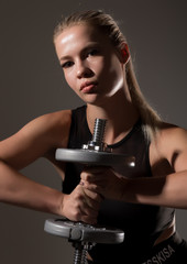 Fitness sexy girl with dumbbells on a dark background. Athlete doing exercises in the gym