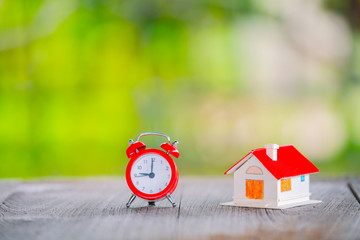 Red house alarm clock placed on a wooden floor The concept of saving and investing a pile of risky coins. The concept of business risk starts with obstacles and risks.