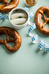 Münchener Weißwurst in Terrine und Brezel mit Oktoberfest Luftschlangen auf Pastell grünen...