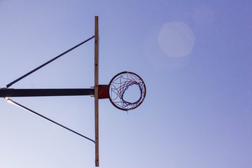  Bottom view of a basketball backboard and ring against a bright blue sky. Sports and basketball games on the sports field. Active lifestyle. Copyspace on the right side of the image.