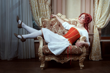 Portrait of a beautiful young woman in a dress and corset. Woman is lying on an armchair.