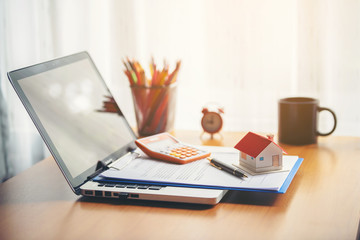 A coffee cup laptop with financial documents on a wooden table by the window.