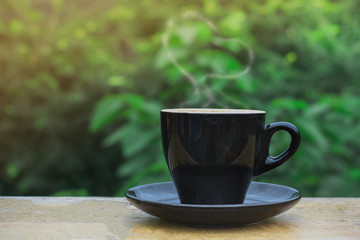 Hot coffee, heart shape smoke in black ceramic cup on wooden table in coffee shop and cafe with green background and flare light, copy space for your text. Times to relax with caffiene concept.