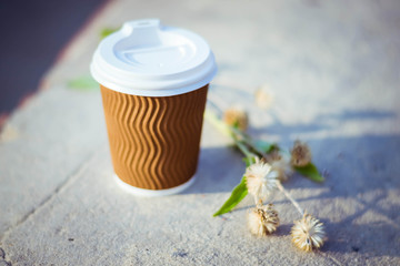Paper cup with coffee. Dry flowers on brown background. Bright summer good morning. A bee flies near a coffee cup. Brown paper cup with plastic white lid.