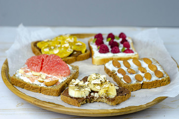 Healthy breakfast toasts with peanut butter, banana, chocolate, chia seeds, raspberries, almond, yogurt, oranges, grapefruit. Wooden plate