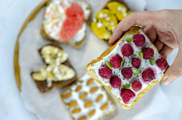 Raspberry and yogurt bread toast in a hand for breackfast. Set with toast bread and different toppings on white wooden background, top view