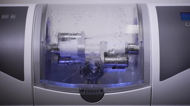 dental CNC machine is making dental implant, rotating, polishing and washing by water flows, closeup view