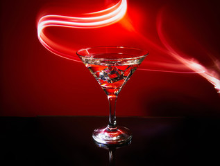 Martini glass isolated on a red background with stripes of neon light painting behind them. Light wave, play of colors, drawing with light.