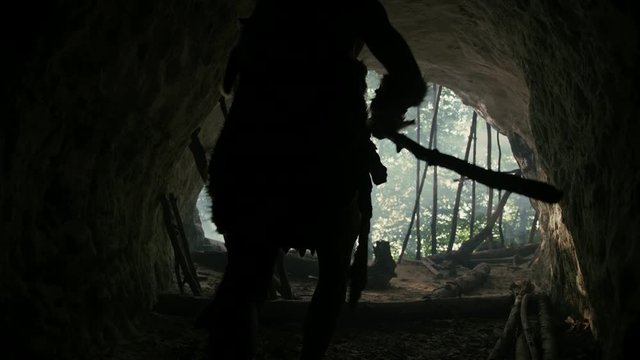 Primeval Caveman Wearing Animal Skin and Fur Holds Stone Tipped Spear Comes out of His Cave into Prehistoric Forest Ready to Hunt. Neanderthal Going Hunting into the Jungle