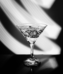 Martini glass isolated on a dark background with stripes of neon light painting behind them. Light wave, play of colors, drawing with light. Black and white