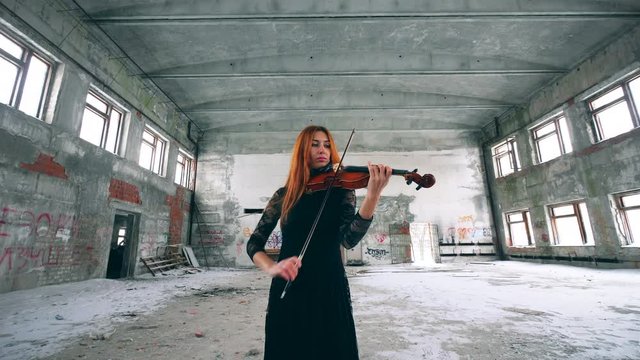 Redhead lady is playing the violin in an abandoned building