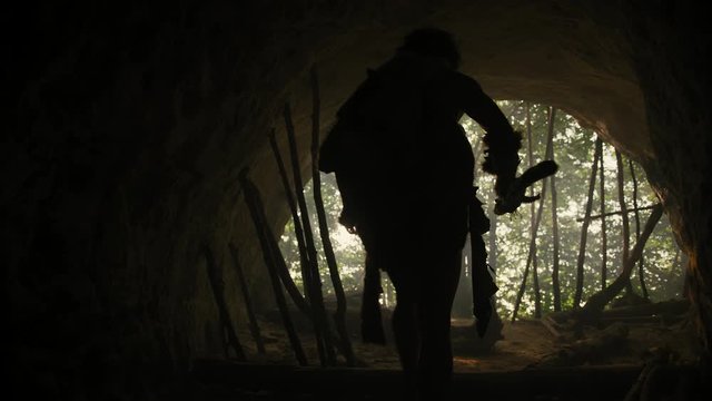 Primeval Caveman Wearing Animal Skin and Fur Holds Stone Tipped Spear Comes out of His Cave into Prehistoric Forest Ready to Hunt. Neanderthal Going Hunting into the Jungle