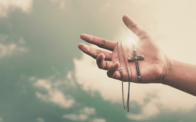 Praying hands hold a crucifix or cross of metal necklace with faith in religion and belief in God on confession background. Power of hope or love and devotion.