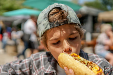 Cute teenage boy eating hot dog and having fun outdoors