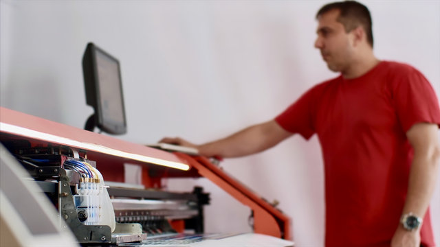 Operator works on computer by setting print options. Typography worker printing production on computerized modern printing press. Printmaker using ciss system for inkjet printer. Publishing industry.