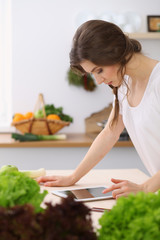 Young woman looking for a new recipe for cooking in a kitchen. Housewife is making online shopping by tablet computer and credit card