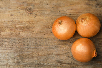 Ripe onions on rustic wooden table, flat lay with space for text