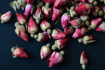 Dried rose buds scattered on a dark surface. Rose tea close up