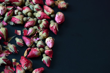 Dried rose buds scattered on a dark surface. Rose tea close up