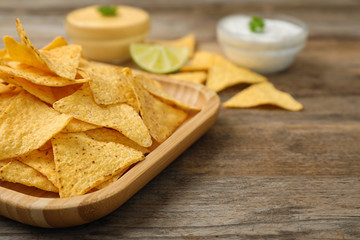 Plate of Mexican nacho chips on wooden table, closeup. Space for text