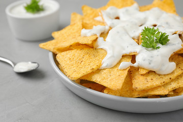 Plate of Mexican nacho chips with sauce on grey table, closeup