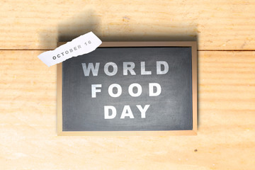 Chalkboard with World Food Day text and ripped paper with the date of October 16 on a wooden background